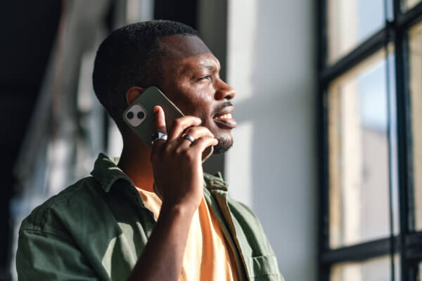 RiPSIM Spec Sheet for eSIMs Cloud-Native Scalable Architecture A man talking on a mobile phone near a window with sunlight streaming in, with a document titled 'RiPSIM Spec Sheet for