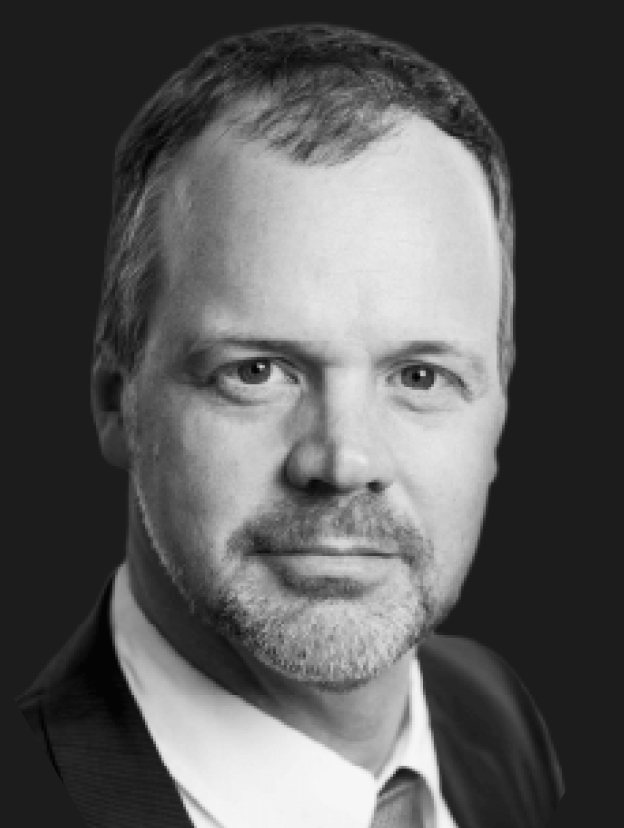 A black-and-white portrait of a man with short hair, a beard, and a serious expression, wearing a suit and tie.